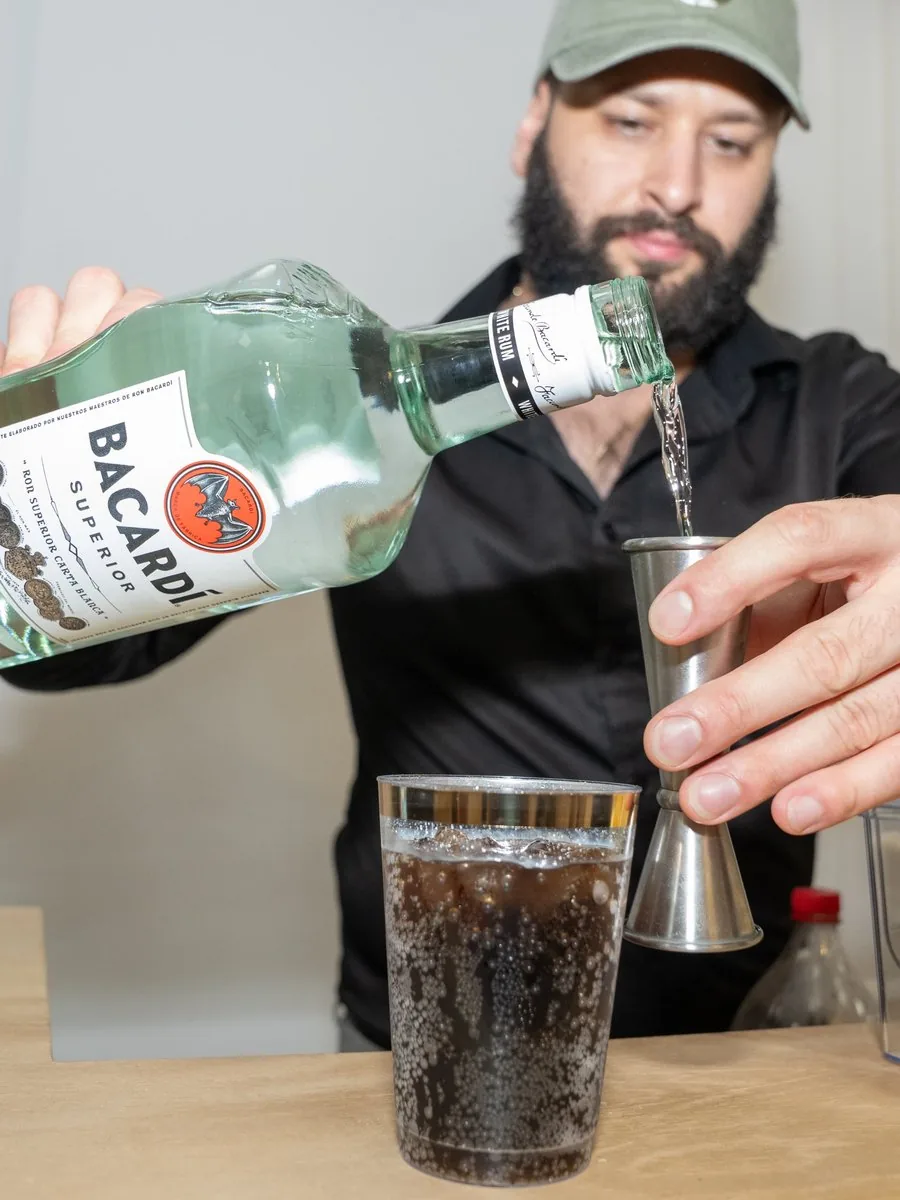 Hernan measuring a pour of white rum with a jigger into a highball